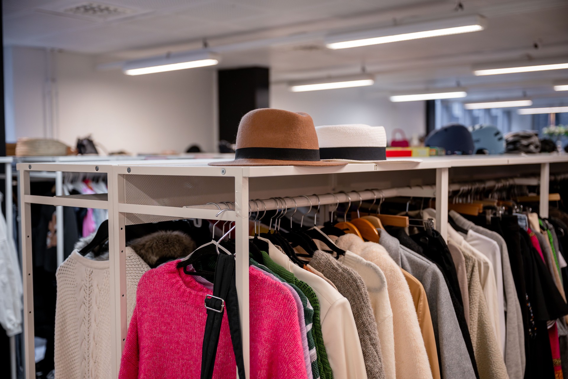 Clothing rack filled with sweaters, jackets, and hats in a thrift store.