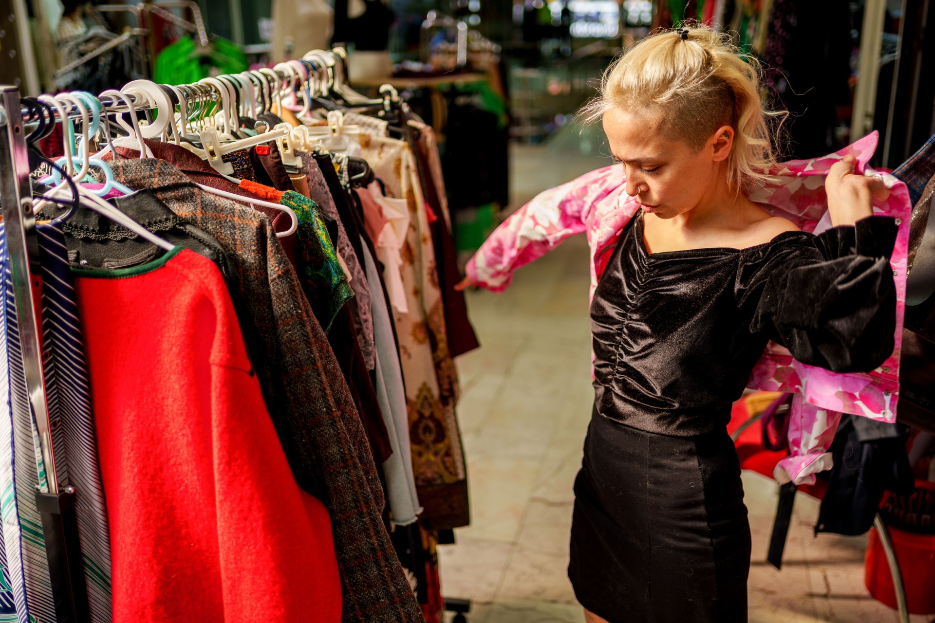 A woman browses through clothing racks filled with second-hand and vintage garments in a store